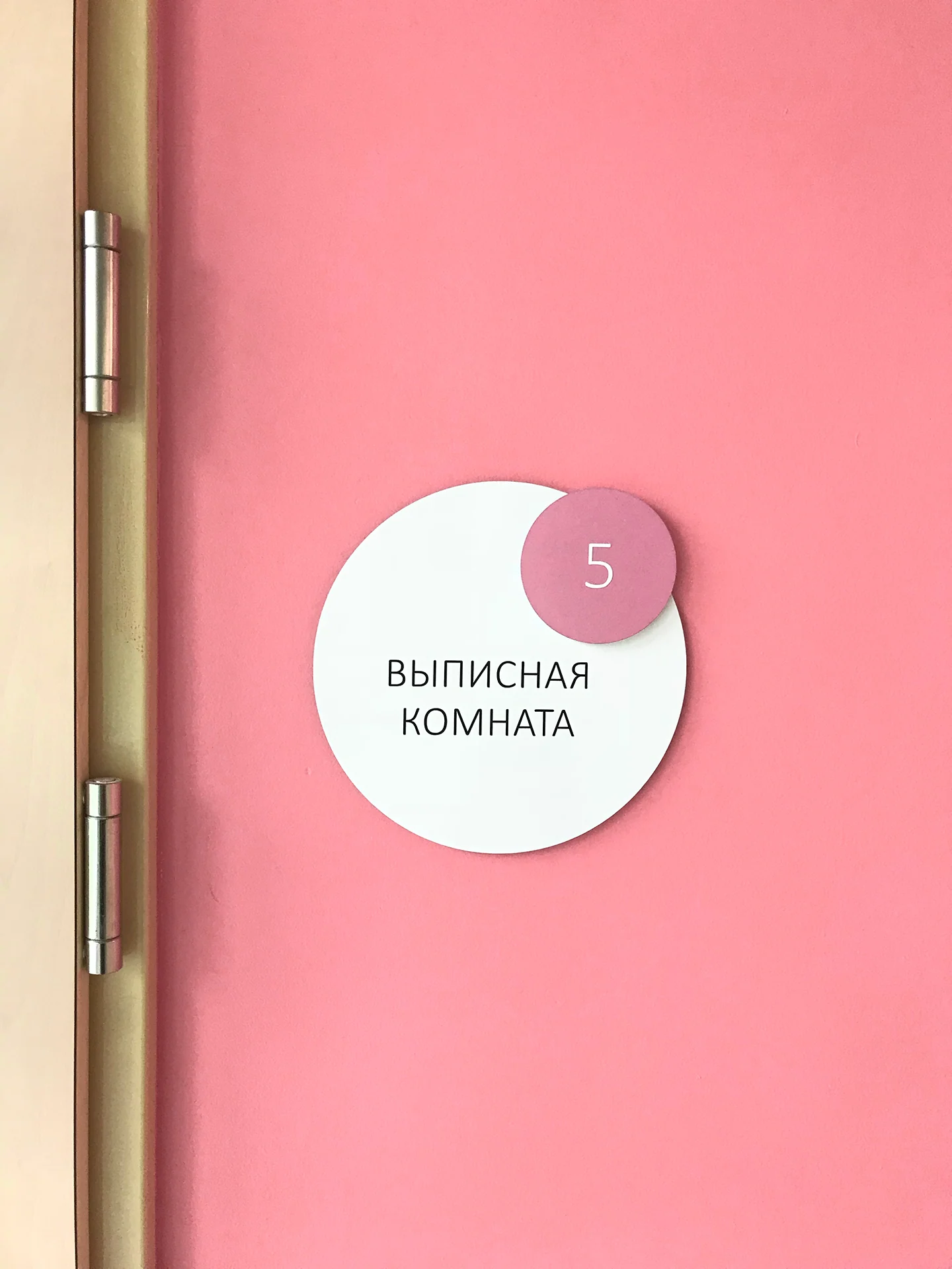 Круглая табличка «Выписная комната» на розовой стене